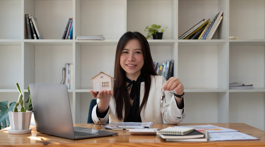 Real estate professional at desk holding house model and keys